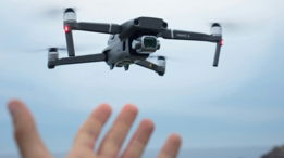 a hand holding a black and white remote control flying over a body of water